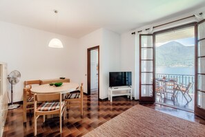 A dining area with a round table and chairs, a TV on a stand, and a view of a mountain through a large sliding glass door.
