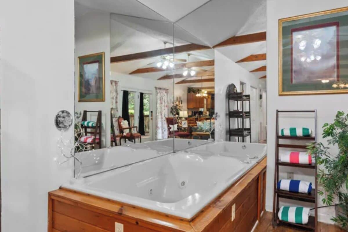 A bathroom with a large bathtub, wooden cabinetry, and a mirror reflecting the room.