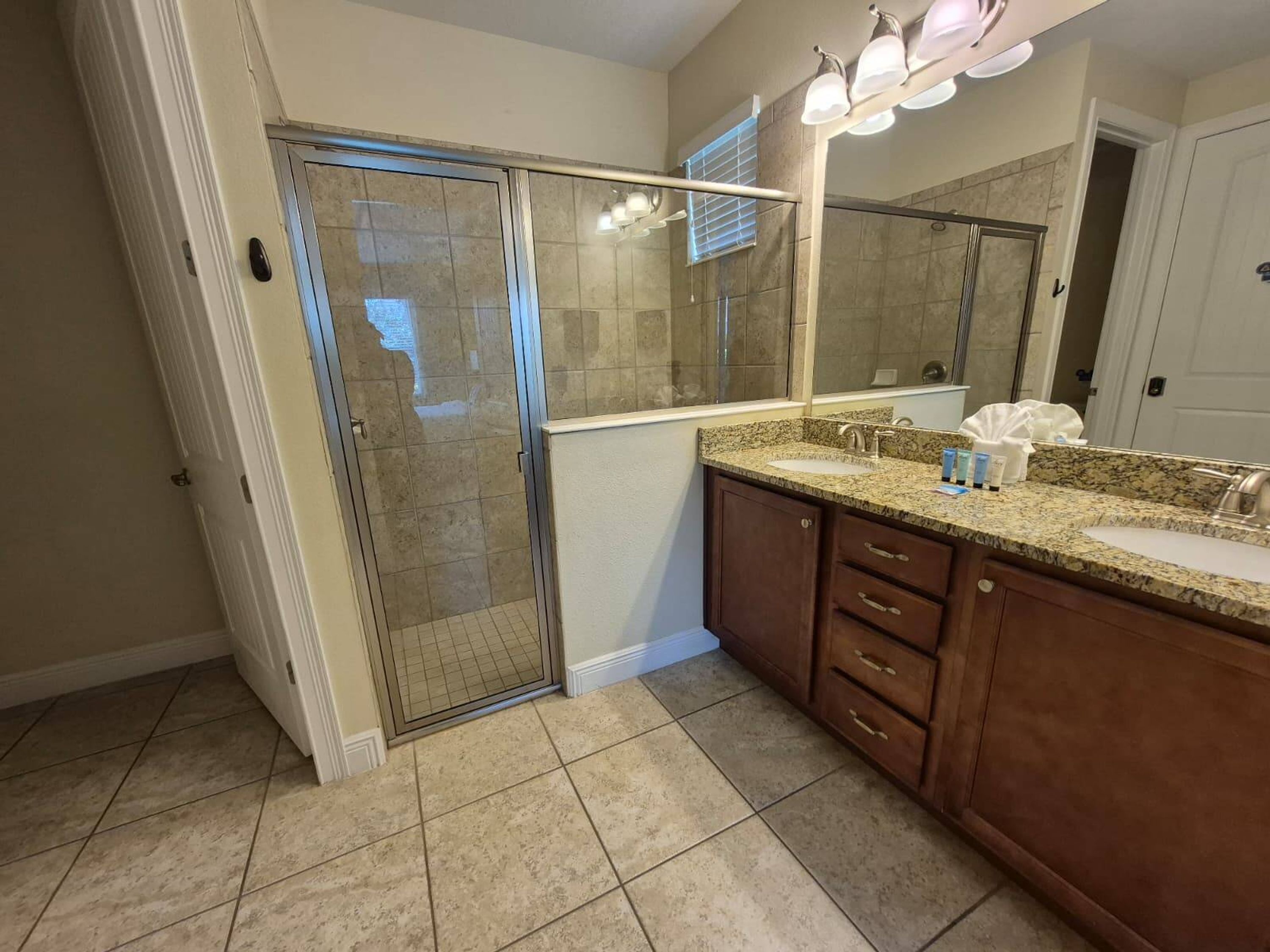 A bathroom with a glass shower door, a vanity with a sink, and a large mirror.