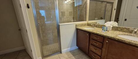 A bathroom with a glass shower door, a vanity with a sink, and a large mirror.