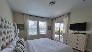 Una camera da letto con un letto grande, una cassettiera, una televisione e un balcone con tende.