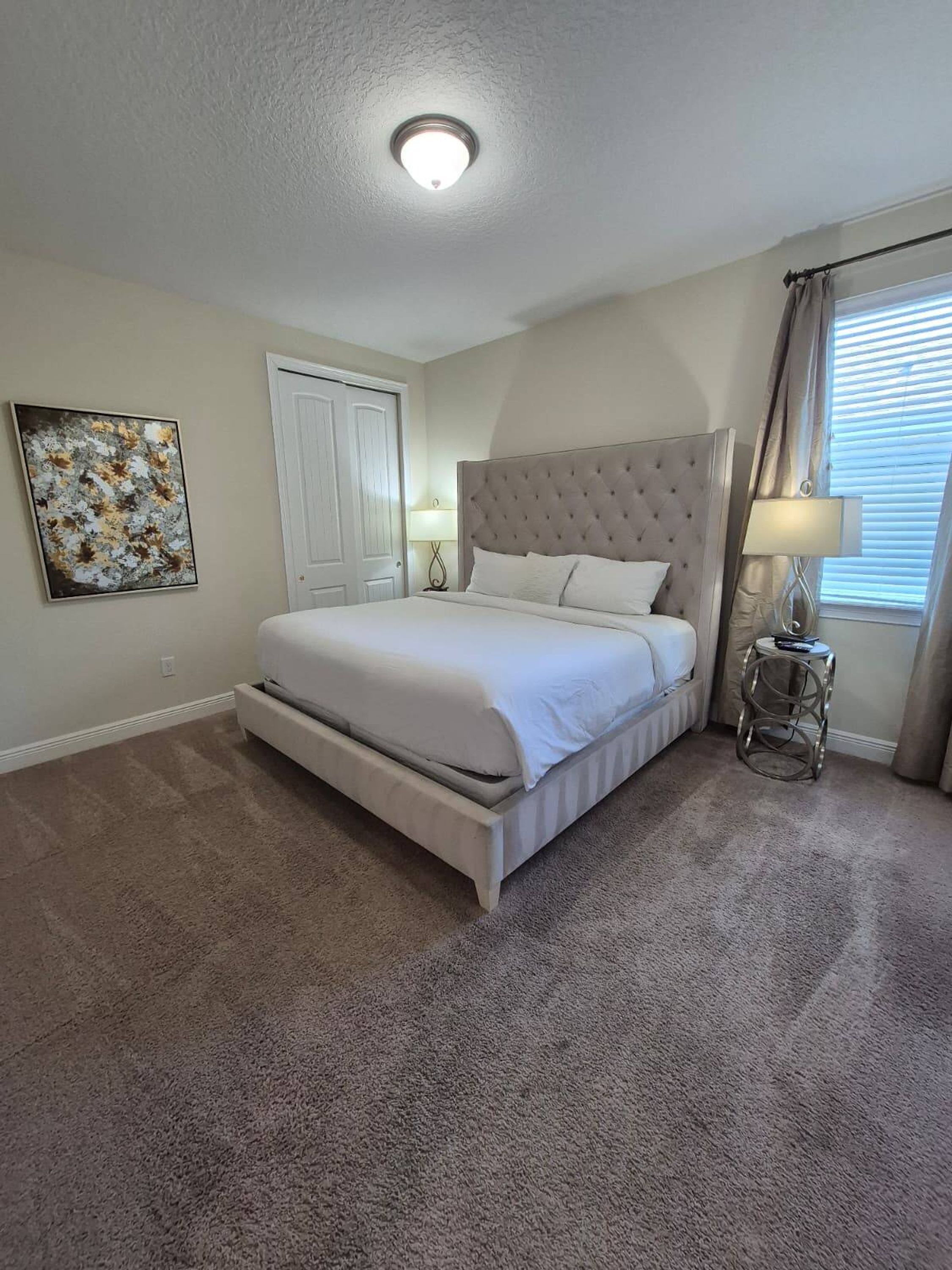 A bedroom with a large bed, two bedside tables, a ceiling light, a door, and a window with curtains.