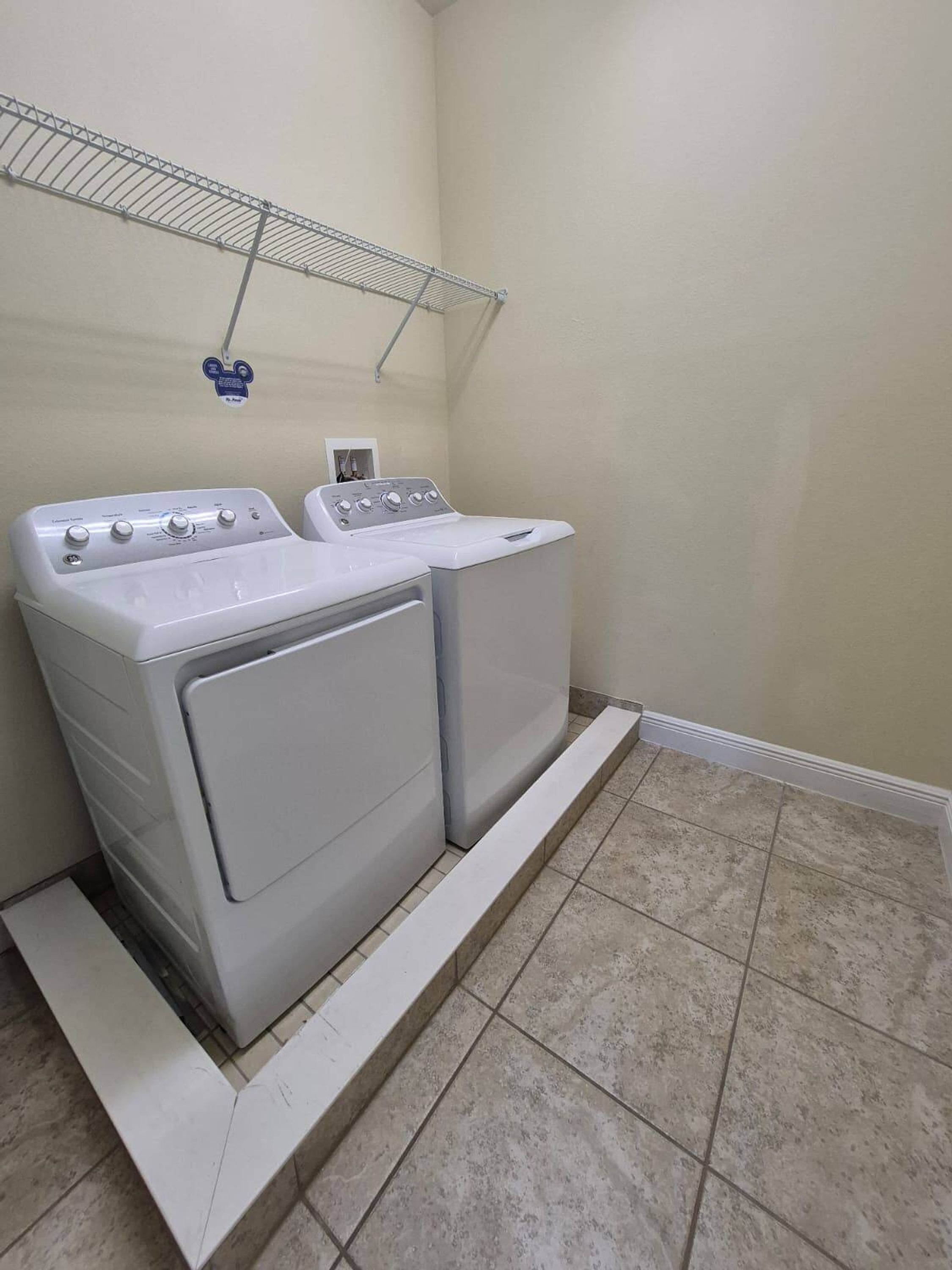 A laundry room with two stacked washers and dryers, a metal shelf above, and a tiled floor.