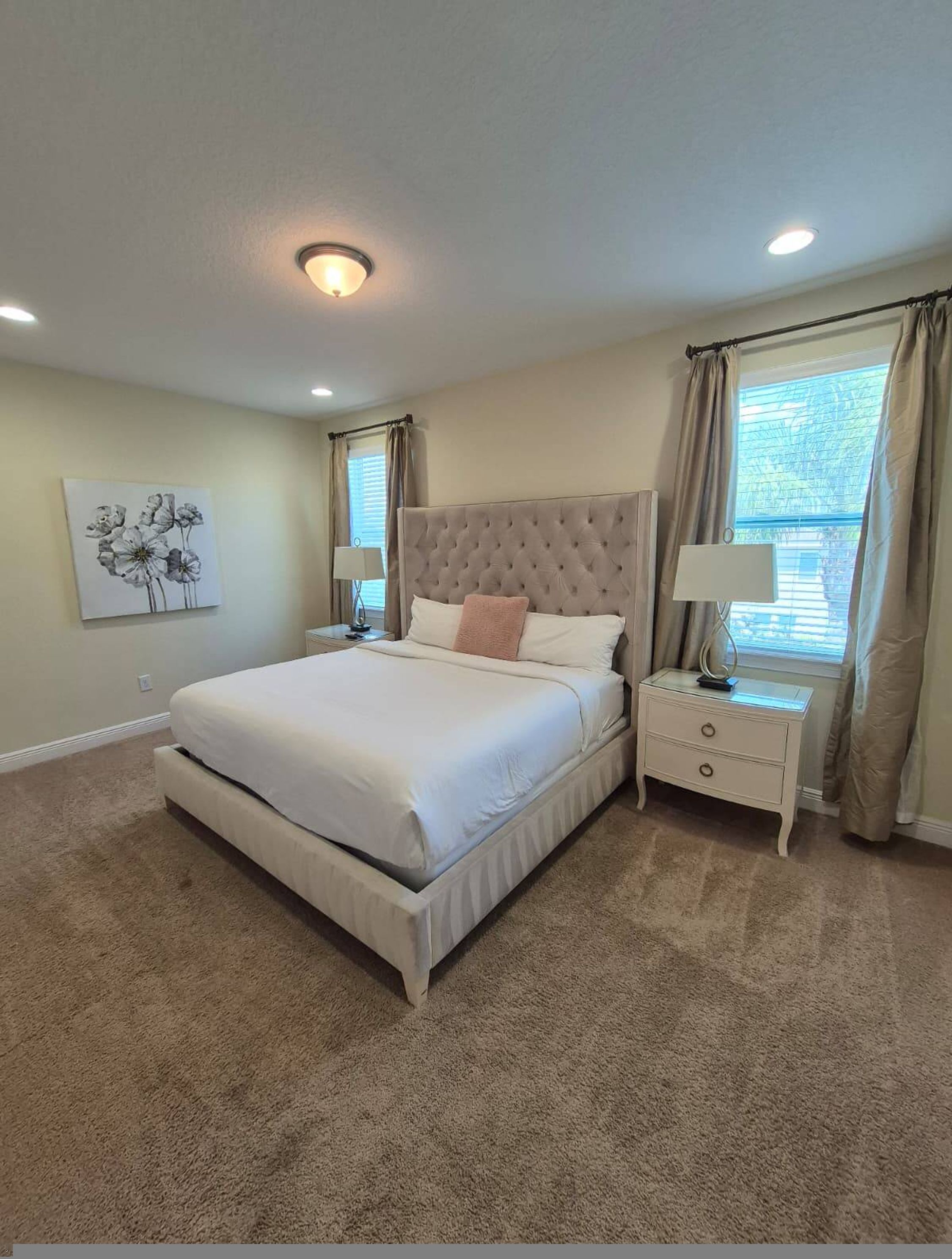 A bedroom with a large bed, two bedside tables, a nightstand, a wall-mounted lamp, and a window with curtains.