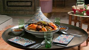 A traditional Moroccan tagine on a tray with a plate of couscous and vegetables, surrounded by patterned dishes and glasses. - A Thousand and One Nights (Tours)