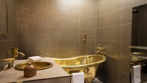 A luxurious bathroom with a gold bathtub, a sink, and a mirror. - A Thousand and One Nights (Tours)