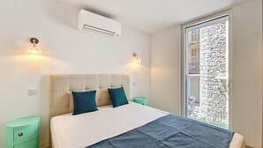 A bedroom with a bed, bedside tables, an air conditioning unit, and a view of a balcony. - N&J - JULIANA EMERAUDE - Central Nice • AC • Walk to beach (Niza)