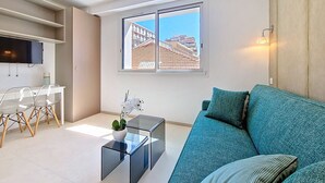 Una sala de estar moderna con un sofá, una mesa de centro de vidrio con una planta y un televisor montado en la pared.