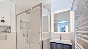 A modern bathroom with a glass-enclosed shower, a white sink, and a mirror.