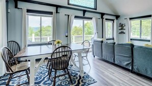 A dining area with a table and chairs, a sofa, and large windows with curtains.