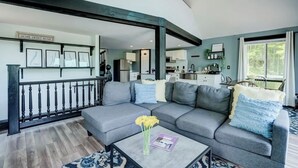 A modern living room with a grey sectional sofa, a coffee table with a magazine, and a view into the kitchen area.
