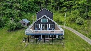 A two-story cabin with a deck, surrounded by lush greenery.