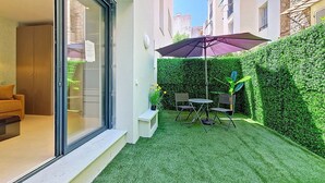 A modern apartment with a glass door entrance, a small patio with a table and chairs, and a neatly trimmed hedge. - N&J - JARDIN CORAIL - Garden • AC • Walk to beach (Niza)