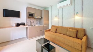 A modern living room with a sofa, a coffee table, and a kitchen area with a microwave and sink. - N&J - JARDIN CORAIL - Garden • AC • Walk to beach (Niza)