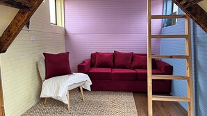 Ein gemütliches Zimmer mit einem roten Sofa, einem weißen Sessel und einer Holzleiter.