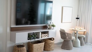 Un salon moderne avec un grand téléviseur à écran plat fixé à un mur blanc, une petite table ronde avec des chaises et des paniers en osier posés sur le sol.
