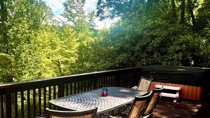 Une terrasse dotée d’une table ronde et de chaises, entourée d’une autre terrasse en bois et d’arbres touffus.