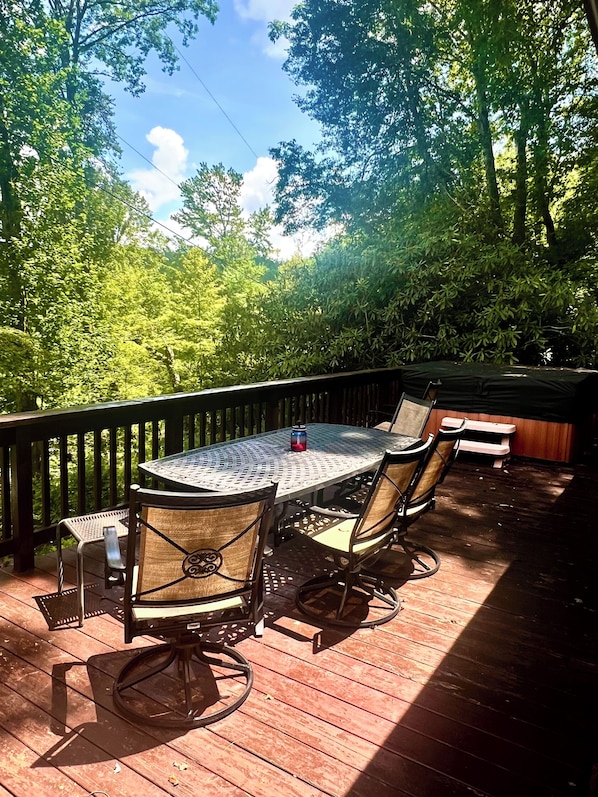A deck with a round table and chairs, surrounded by a wooden deck and dense trees.