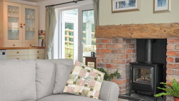 A cozy living room with a grey sofa, a brick fireplace, and a wooden ceiling. - Upper Court Cottage (Bude)