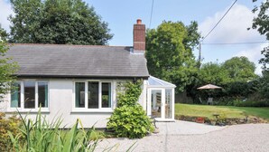 A house with a gravel driveway, a conservatory, and a garden with a patio area. - Upper Court Cottage (Bude)
