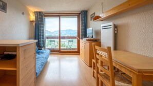 A room with a bed, a desk, a chair, a television, and a view of mountains through a large window. - Studio Apartment 'Avec Vue Splendide' with Mountain View and Balcony (Villarembert)
