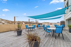 An outdoor patio with blue chairs and tables, a wooden deck, and a view of the beach. - Romar Beach 105 (Orange Beach)