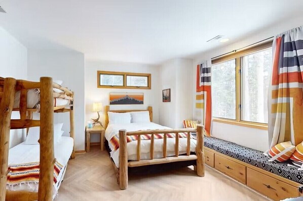 A room with bunk beds, a wooden bed, a bedside table with a lamp, a window with curtains, and a wall-mounted picture. - Benchmark-Curate Telluride, Ski in/Out, Private, Hot Tub, Views, Fireplace (Mountain Village)