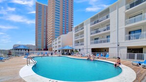 A pool area with a wooden deck, lounge chairs, and a view of tall buildings in the background. - Sugar Beach 238 (Orange Beach)