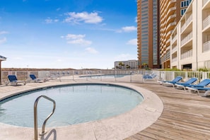 A pool area with lounge chairs, a pool, and a high-rise building in the background. - Sugar Beach 238 (Orange Beach)