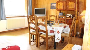 A dining area with wooden chairs and a table, a television, and a cabinet with a clock. - Family apartment for 6 people in a quiet residence in Sainte Marie (Vars)