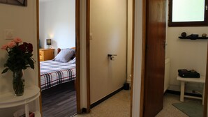 A narrow hallway leading to a bedroom with a bed, a bedside table with a vase of flowers, and a window with a view. - Family apartment for 6 people in a quiet residence in Sainte Marie (Vars)
