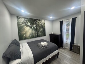 A bedroom with a bed, a nightstand, a wall-mounted picture, and a window with curtains. - Spacious 4-bedroom apartment in brilliant Bristol with AC (Bristol)