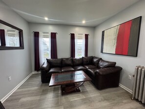 A living room with a brown leather sectional sofa, a glass-top coffee table, and a large abstract painting on the wall. - Spacious 4-bedroom apartment in brilliant Bristol with AC (Bristol)