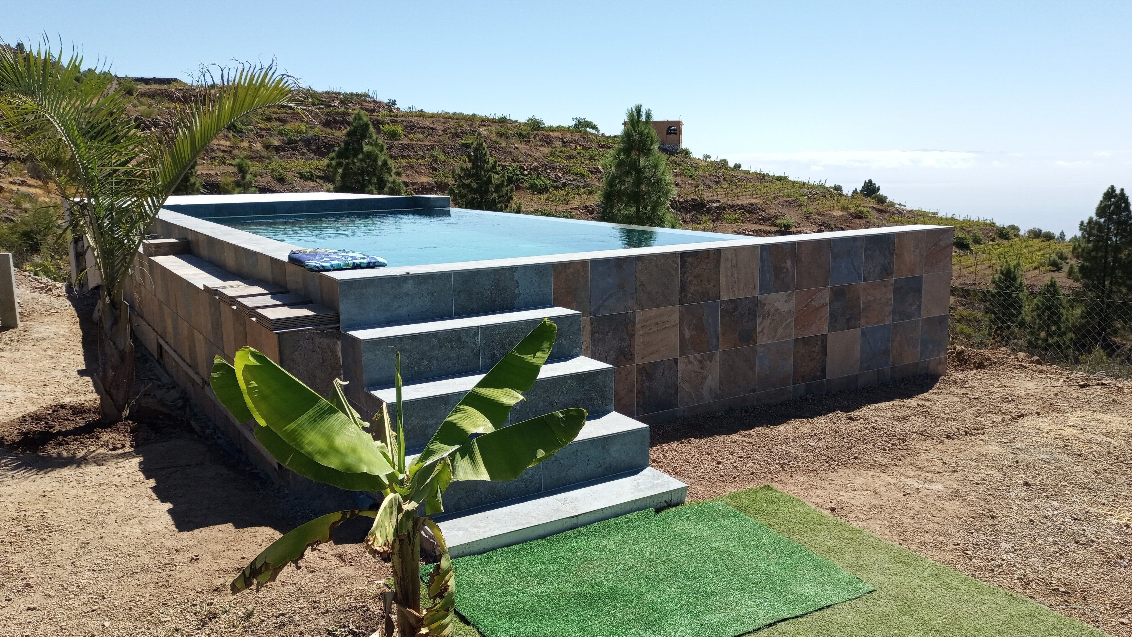 A swimming pool with a stone exterior and steps leading into it, surrounded by a natural landscape.