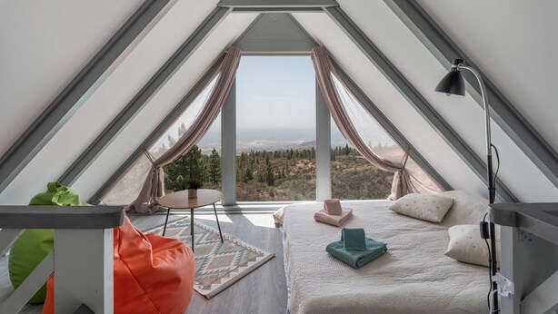 A bedroom with a large window, a bed, a desk, and a chair.