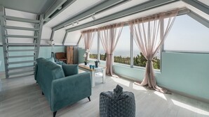A modern loft bedroom with a skylight, a sofa, a small table, and a view of the landscape.