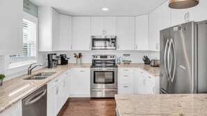 A modern kitchen with white cabinetry, stainless steel appliances, and a granite countertop. - Updated 5 BR Canal Home, Short Walk To Beach! (Ocean Isle Beach)
