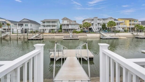 A waterfront property with multiple buildings, a dock, and a clear view of the water. - Updated 5 BR Canal Home, Short Walk To Beach! (Ocean Isle Beach)