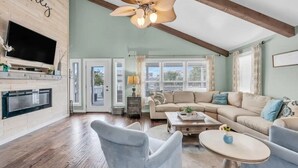 A spacious living room with a fireplace, a television, and a ceiling fan. - Updated 5 BR Canal Home, Short Walk To Beach! (Ocean Isle Beach)