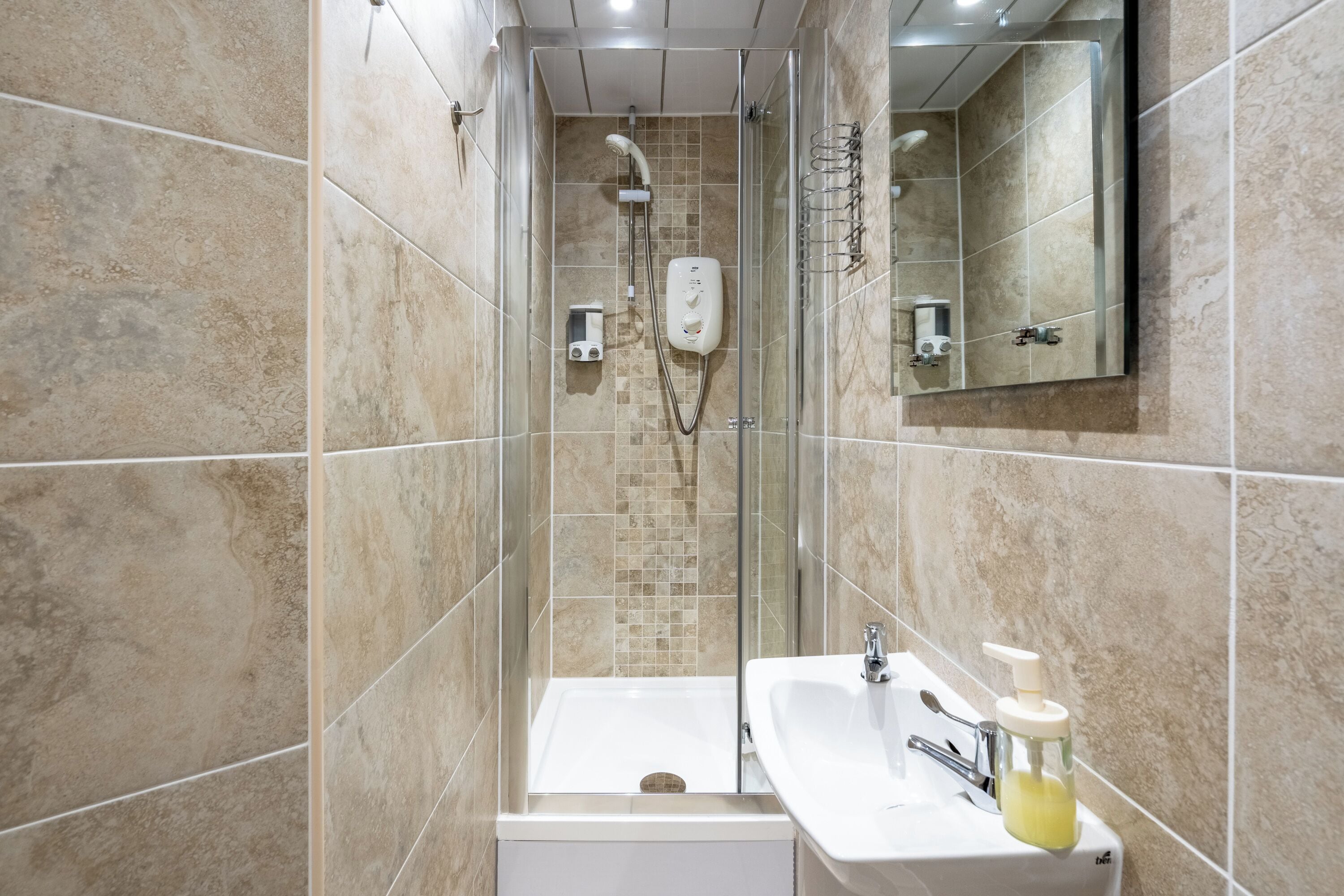 Une salle de bain moderne avec une douche à parois de verre, un lavabo blanc doté d’un distributeur de savon et un miroir au-dessus du lavabo.
