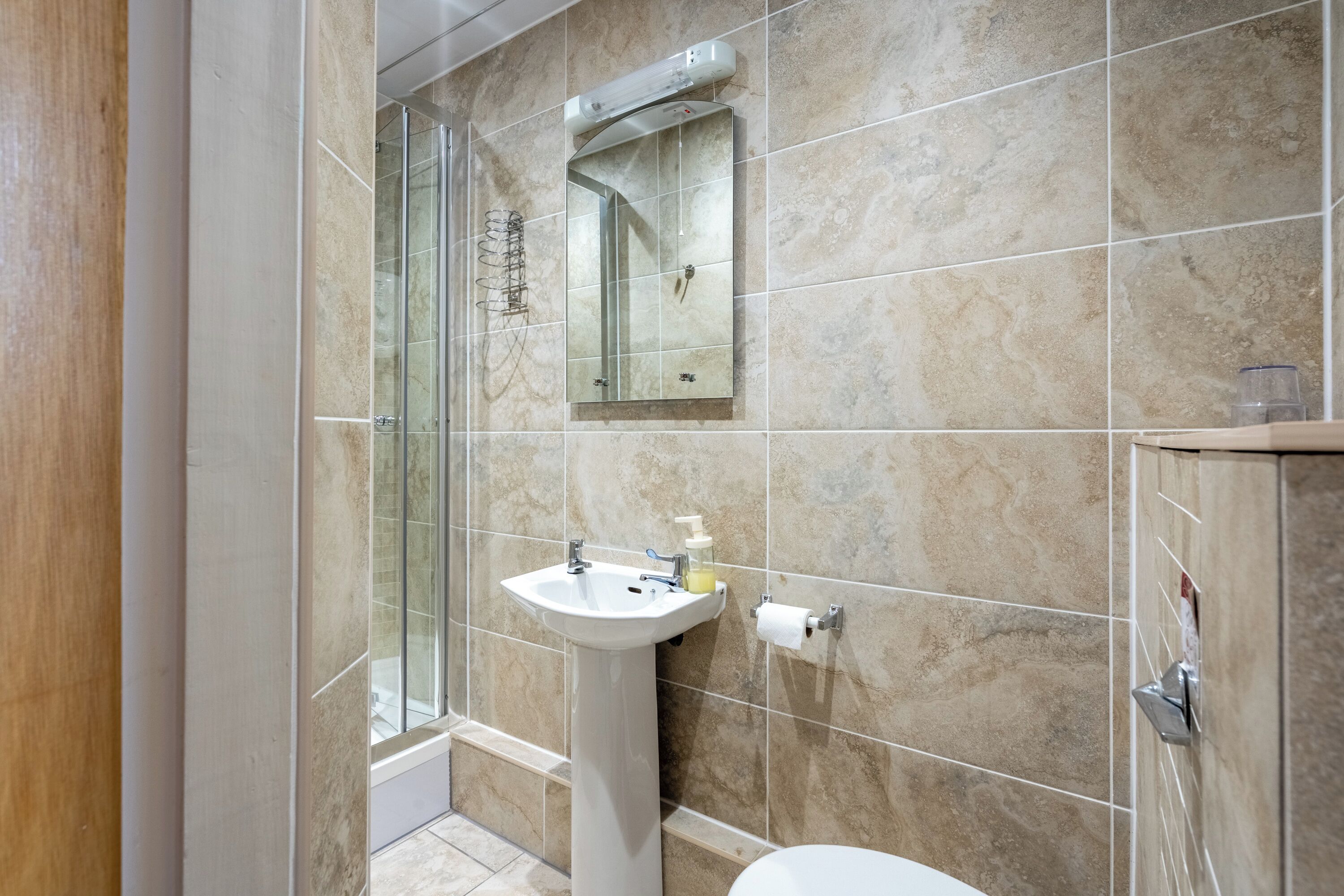 A bathroom with a glass shower enclosure, a pedestal sink, and a toilet.