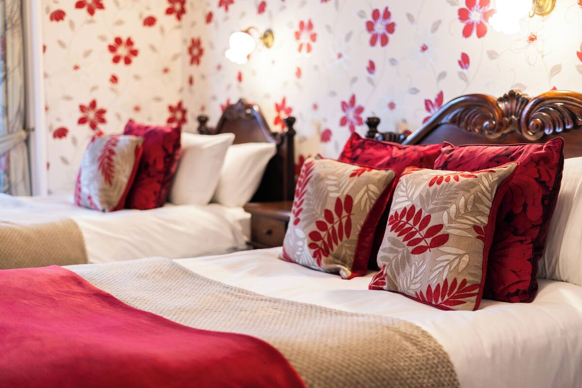 Ein Hotelzimmer mit zwei Betten, blumigem Wandpapier und Bettwäsche in Rot und Beige.
