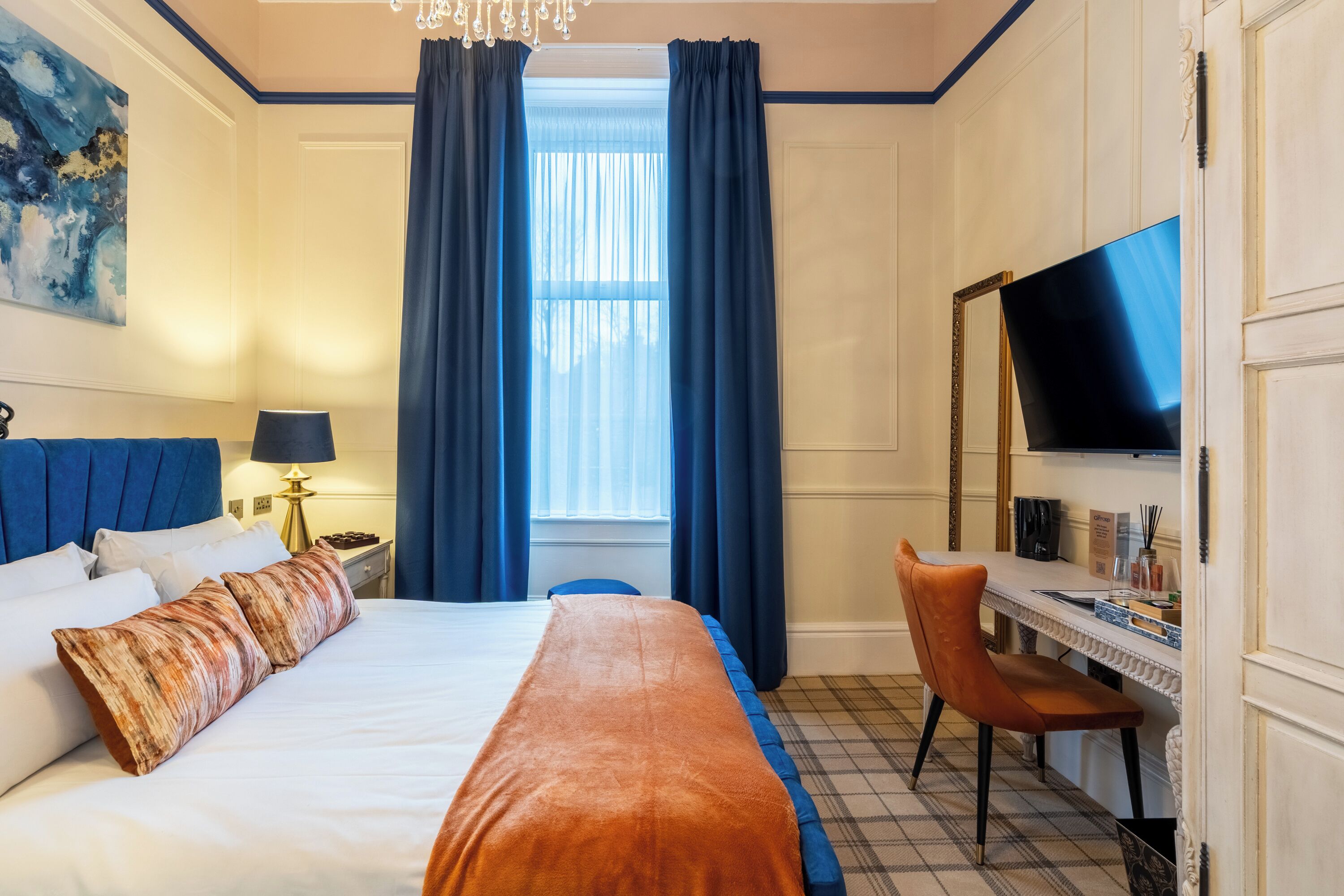 Une chambre d’hôtel avec un grand lit, un bureau avec une chaise, une télévision et une fenêtre avec des rideaux.