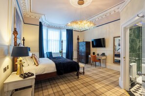 Quarto de hotel com uma cama grande, uma escrivaninha, uma televisão e banheiro com piso de mármore.