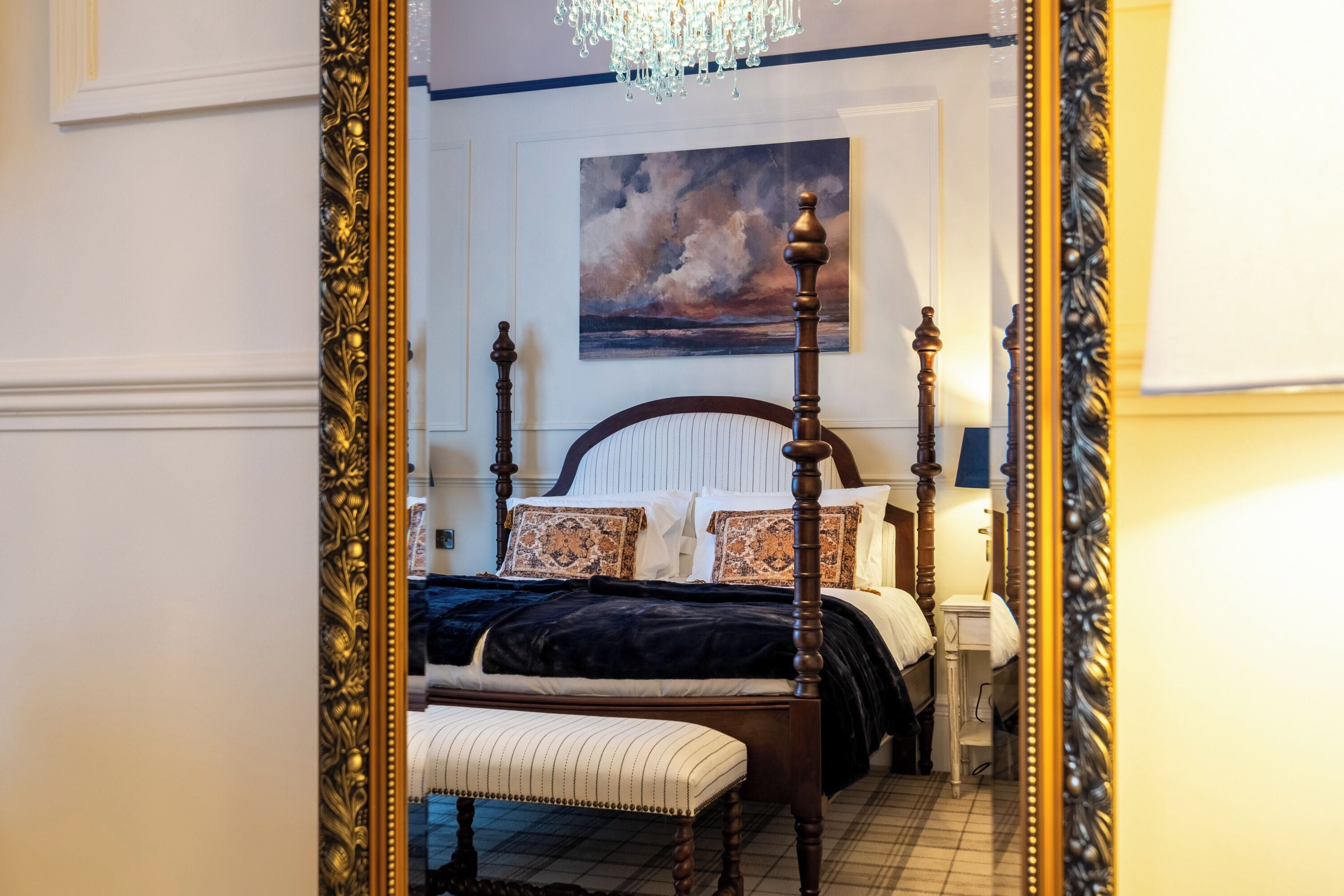 A bedroom with a four-poster bed, a bench, a nightstand, and a painting on the wall.