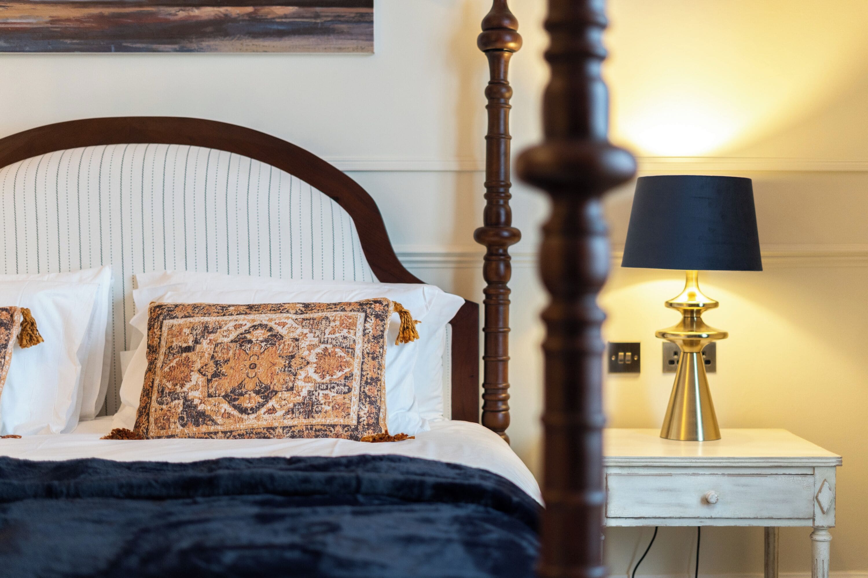 A neatly made bed with a patterned throw, a bedside lamp, and a small white nightstand.