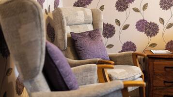 A chair with a cushion, a wooden side table, and a wall with floral wallpaper.