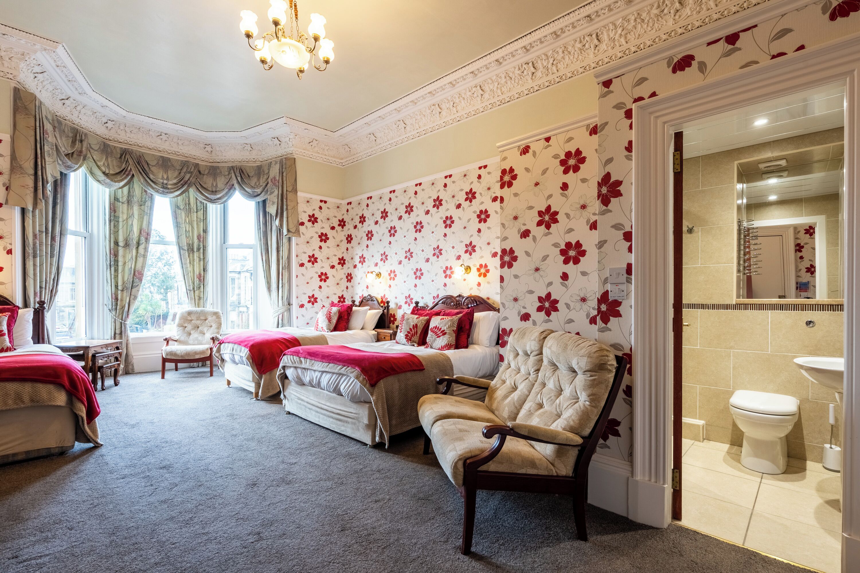 A bedroom with two beds, a sitting area with a chair, and a view of the bathroom.