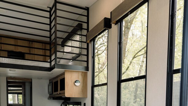 A modern RV interior with a sofa, a kitchenette, and large windows.