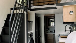 A compact living space with a staircase, a washing machine, a sink, and a couch.